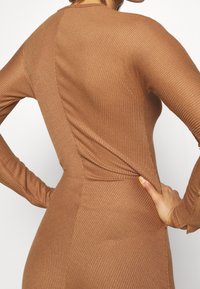 Abito a tubo marrone a coste con maniche lunghe, caratterizzato da una texture sottile e una cucitura diagonale sul retro. Tessuto liscio e elasticizzato.