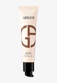 Rør med Armani Skin Tint, beige med svart pumpe-dispenser, som har merkevaren sitt logo i brunt. Teksten inkluderer "langvarig & pleie." Glatt finish.
