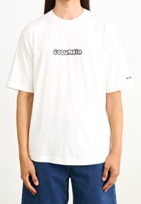 Camiseta de algodón blanca con mangas cortas y escote redondo, con un logo negro de 'COLUMBIA' impreso en la parte delantera.