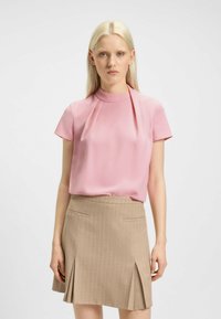 Blusa rosa a maniche corte con collo alto, realizzata in tessuto morbido, abbinata a una gonna a righe sottili color marrone chiaro con spacco frontale e tasche.