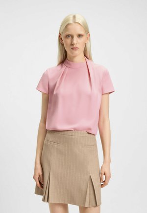 Blusa rosa a maniche corte con collo alto, realizzata in tessuto morbido, abbinata a una gonna a righe sottili color marrone chiaro con spacco frontale e tasche.