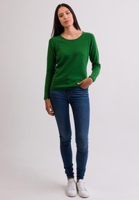 Grön långärmad stickad tröja med rund halsringning, tillsammans med blå skinny jeans och vita sneakers. Enkelt mönster, inga mönster eller accenter.