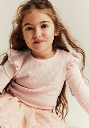 Lyserød ribbet langærmet trøje med blonder og flæser ved skuldrene, kombineret med et blødt lyserødt luftpagt lagdelt tylskørt. Tekstureret stof.