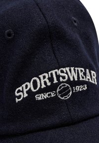 Mörkblå filtkeps med vit broderad text "SPORTSWEAR" och en tennisbollgrafik samt "SINCE 1923" under.