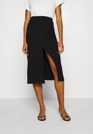 Jupe midi noire côtelée avec une fente à l'avant, dotée d'une taille haute. Associée à un t-shirt blanc uni et des sandales à semelles glissantes à imprimé animal.