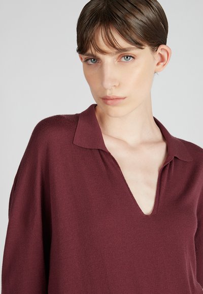 Burgundowa dzianinowa bluzka z dekoltem w kształcie litery V i kołnierzykiem. Miękka tekstura z luźnym krojem, z opadającymi szwami na ramionach i minimalnymi detalami.