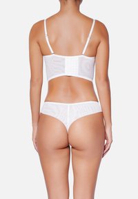 Ensemble bralette et thong blanc, mettant en avant un tissu transparent, des bretelles réglables et une fermeture arrière à crochet et œillet. Design lisse et minimal.
