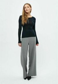 Schwarzes Langarmoberteil mit Rundhalsausschnitt, kombiniert mit hellgrauen weiten Hosen. Die Schuhe sind spitze schwarze Absatzschuhe.
