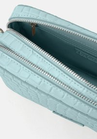 Helles, blaues Handtasche mit Krokodilprägung, metallischen Reißverschlüssen und zwei Fächern. Das Innere zeigt einen glatten Stofffutter.