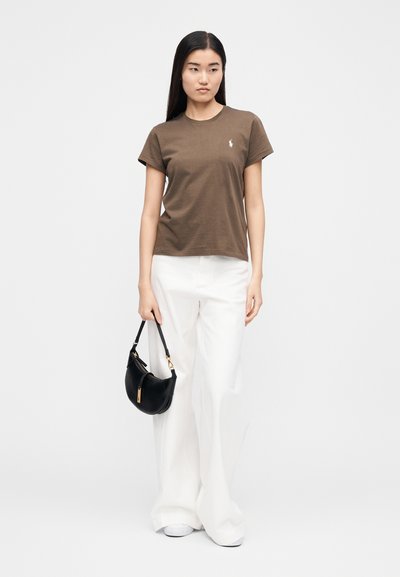 Barna pamut rövid ujjú póló kerek nyakkivágással, fehér bőszárú nadrággal és fekete válltáskával párosítva.