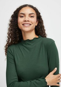 Långärmad, ribbad topp i mörkgrön med hög halslinning och volangärmar, tillverkad av ett mjukt och stretchigt tyg.