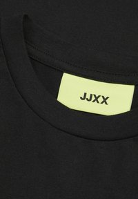 Crni pamučni T-shirt s okruglim izrezom. Oznaka u neon žutoj boji s crnim tekstom "JJXX" vidljiva unutar ovratnika. Glatka tekstura.