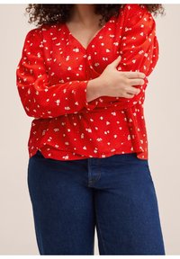 Blouse à motifs floraux rouges avec des manches longues, un col en V et une coupe décontractée ; associée à un jean bleu foncé au design classique.