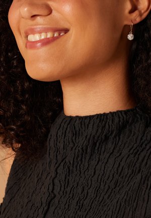 Boucle d'oreille en or avec un charme sphérique texturé ; modèle portant un haut en tissu noir froissé avec un col montant.
