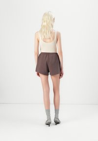 Beige tank top, brune mønstrede shorts og grå sokker sammen med lyse sko. Outfittet har en elastisk midje og en avslappet passform.