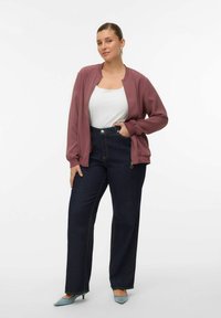 Lichtgewicht mauve bomberjack over een wit topje, gecombineerd met donkerblauwe jeans met hoge taille. Lichtblauwe, puntige hakken maken de outfit compleet.