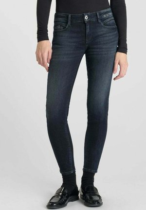 Donkerblauwe skinny jeans met een lichte vervaging, vijf-pocket ontwerp en metalen knoopsluiting, aangevuld met zwarte instappers en een getailleerde top.