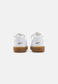 Λευκά δερμάτινα αθλητικά παπούτσια με σόλα από καουτσούκ γκαμ, με μινιμαλιστικό σχέδιο και μία μικρή λεπτομέρεια λογότυπου σε μπλε και κόκκινο στον τακούνι.