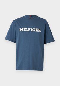 Sininen puuvillapaita pyöreällä kaula-aukolla ja lyhyillä hihoilla. Etuosassa on paksuilla valkoisilla kirjaimilla "HILFIGER"-teksti.