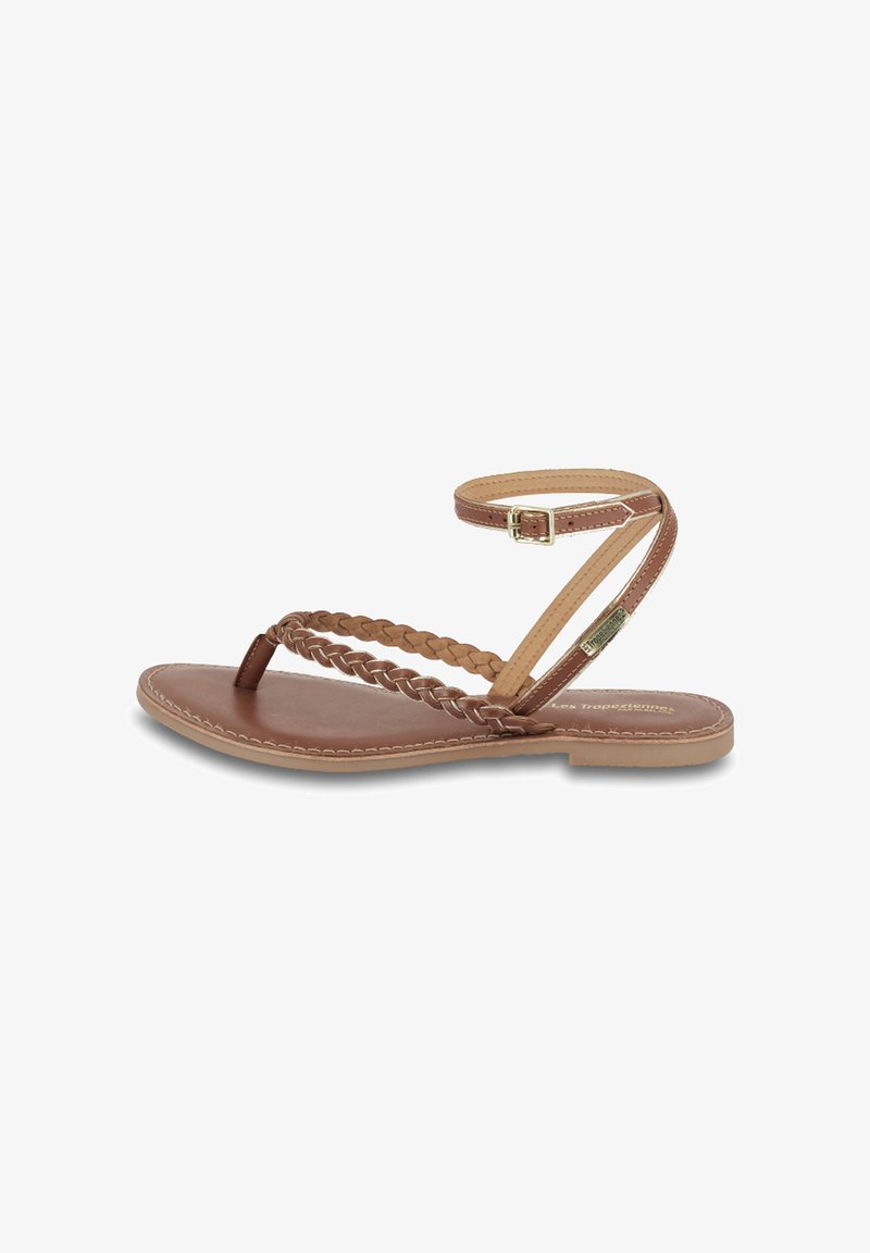 Sandales plates en cuir marron avec une sangle tressée au niveau des orteils, une sangle de cheville avec une boucle et une semelle cousue.