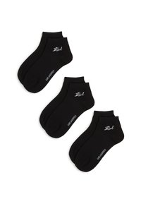 Trīs melnu potīšu zeķu pāri ar baltu "Karl Lagerfeld" logo, sakārtoti diagonāli uz baltā fona.