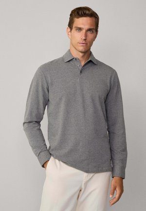 Polo gris à manches longues avec une texture subtile, patte de boutonnage à trois boutons et col ribyré, porté avec un pantalon de couleur claire.