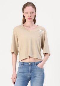 Beige cropped t-shirt with a V-neckline, short sleeves, and a palm leaf design in white. Soft cotton material, casual fit.