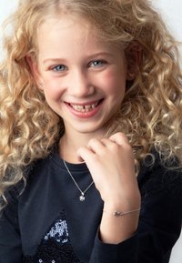 Les bijoux en argent comprennent un pendentif avec un petit charme et un bracelet délicat. L'enfant porte une chemise sombre avec un motif de chat en sequins.