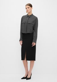 Zwarte pencil skirt met een voor_split, gecombineerd met een cropped grijs gestreept shirt met twee borstzakken, gedragen met zwarte puntige hakken.