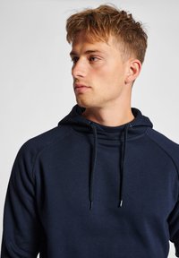 Navyblaues Kapuzenshirt aus weichem Stoff mit einer vorderen Kängurutasche, Kordelzugkapuze und gerippten Bündchen und Saum. Raglanärmel ermöglichen Bewegungsfreiheit.