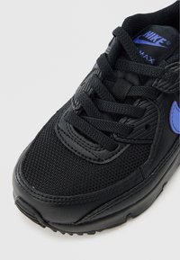 Črni Nike Air Max copat z zgornjim delom iz mrežastega materiala in usnja, teksturiranimi detajli, vijoličnimi poudarki in klasičnim zavezovanjem z vezalkami.