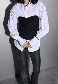 White button-up shirt layered over a black corset-style top, paired with shiny, dark grey, glittery pants. Smooth fabric texture noted.