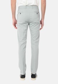 Pantaloni grigi chiari con una vestibilità slim, dotati di tasche posteriori con chiusura a bottone e un tessuto liscio e strutturato. Scarpe con suole a contrasto.