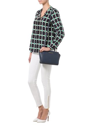 Sort bluse med grønt geometrisk mønster, hvide skinny jeans med lynlåsdetaljer og en navy håndtaske. Modellen bærer hvide spidse hæle.