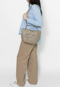 Beige leren handtas met een ronde vorm, zilverkleurige hardware en een buitenzak met ritssluiting. Te dragen op de schouder met een hengsel.