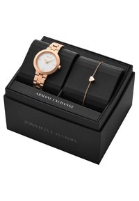 Roséguld klocka med en rund vit urtavla och länkarmband, tillsammans med ett delikat roséguldarmband med ett hjärtanhang, presenterat i en svart låda.