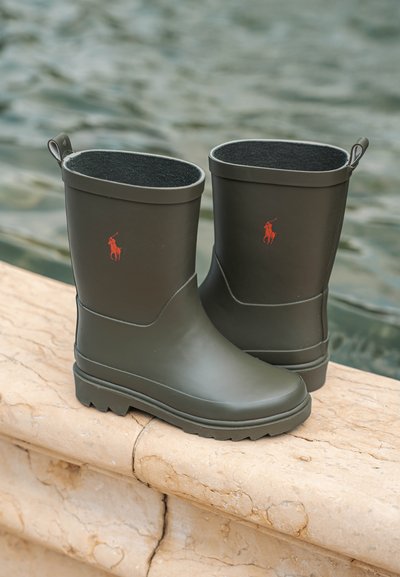 Des bottes en caoutchouc vert foncé imperméables sont dotées d'un intérieur noir texturé et d'un petit logo polo rouge. La semelle présente un motif de crampons dentelés pour une meilleure adhérence.