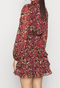 Blumiges Mini-Kleid mit langen Ärmeln, auf schwarzem Hintergrund, mit Rüschensaum und Mustern aus roten, rosa und beigefarbenen Blumen. Hergestellt aus transparenter Stoff.