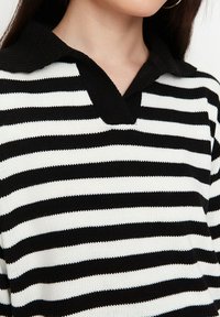 Sweter w czarno-białe paski z teksturowanym wzorem dzianiny, z czarnym kołnierzykiem i dekoltem w kształcie litery V.