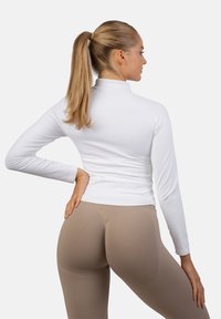 Valkoinen pitkähihaiseen toppi, jossa on korkea kaulus, yhdistettynä beigeihin leggings-pöksyihin, joissa on tekstuuriset yksityiskohdat ja saumaton muotoilu.