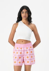 Biely rebrovaný crop top s jedným plecom; ružové háčkované šortky s kvetinovými motívmi v oranžovej a bielej farbe, so zúženým okrajom a elastickým pásom.