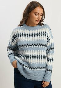 Maglione blu lavorato a maglia con motivi geometrici bianchi e neri. Collo rotondo, polsini e orlo a coste. Tessuto morbido, vestibilità comoda.