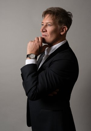 Elegantna ručna sat s srebrnim brojčanikom i crnim kožnim remenom, nošena na ruci u odijelu, ističući oštar, krojeni crni sako.