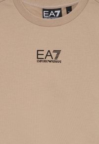 Camiseta beige con cuello redondo que presenta el logotipo negro de EA7 Emporio Armani centrado en el pecho.