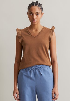 Brown, sleeveless V-neck top with ruffle accents on shoulders, made from soft fabric; paired with light blue, drawstring waist pants.
