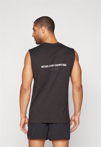 Black sleeveless cotton tank top with "NEVER STOP COMPETING" text in white on the back, featuring a round neckline and a loose fit.