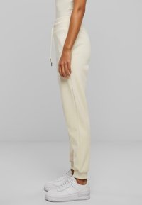 Pantalones jogger color crema con cintura ajustable y tobillos ajustados, combinados con zapatillas blancas, mostrados en una vista lateral.