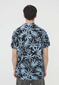 Maglietta a maniche corte in tessuto nero con una fantasia di foglie tropicali blu, dotata di un colletto classico e di una vestibilità rilassata.
