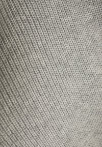 Světlé šedé pletené tkaniny s ribbovanou texturou. Vzor se vyznačuje konzistentními vertikálními liniemi a měkkým povrchem.