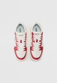 Hvite sneakers med røde lærdetaljer, perforert tå og hvite snøringer. Har "REPLAY"-logoen på tungen og siden.